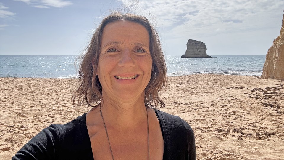 Mandy Ahlendorf am Strand an der Algarve, mit Meer und Felsen im Hintergrund